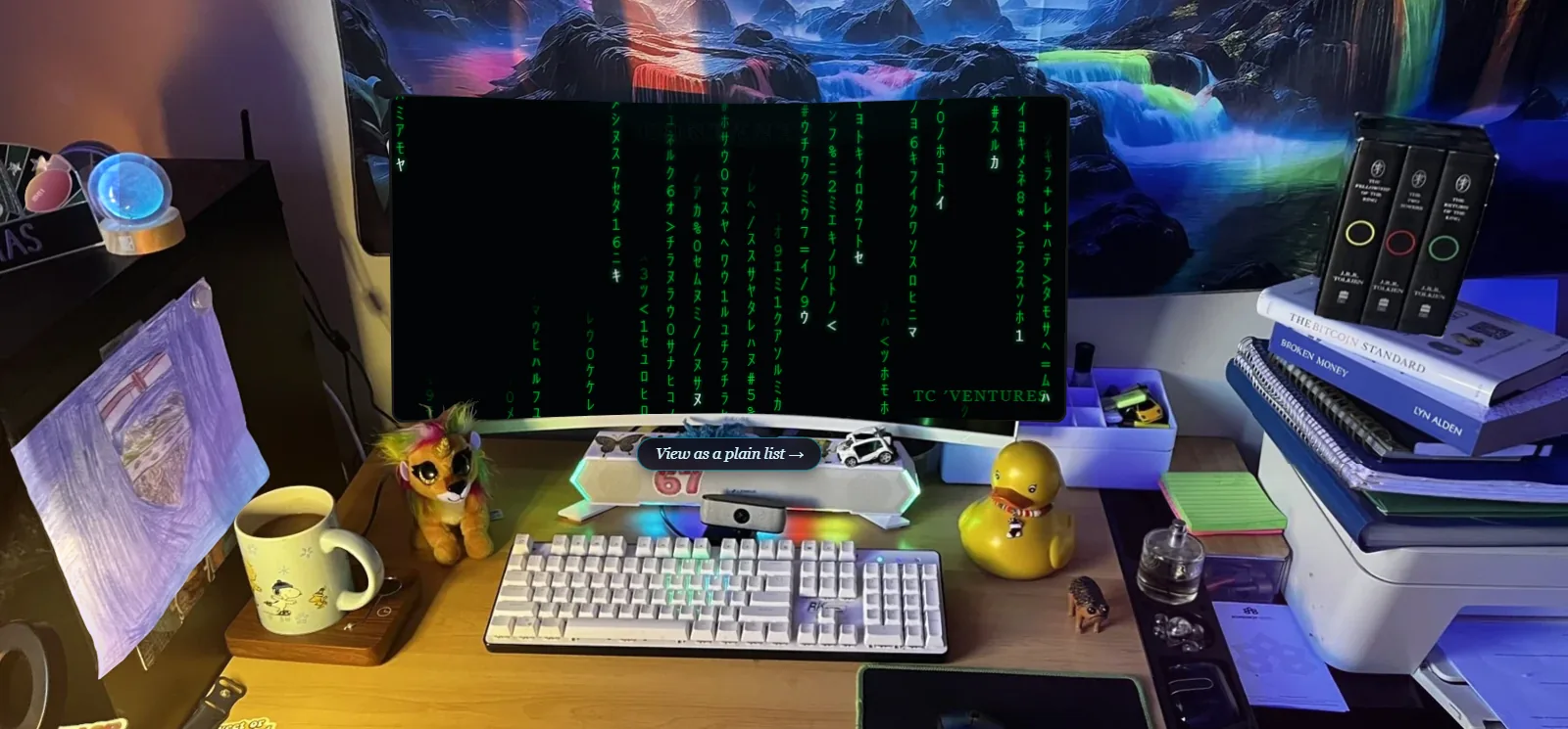 A photograph of a home-office desk used as a website menu: a wide curved monitor running a screensaver of falling green characters signed TC 'Ventures, a lit mechanical keyboard, a mug, a small stuffed toy, a rubber duck and a stack of books, with a small on-screen pill reading View as a plain list.